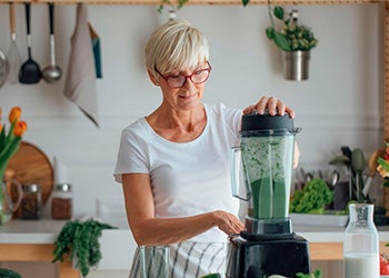 Mulher preparando um suco verde fresco na cozinha, representando hábitos saudáveis